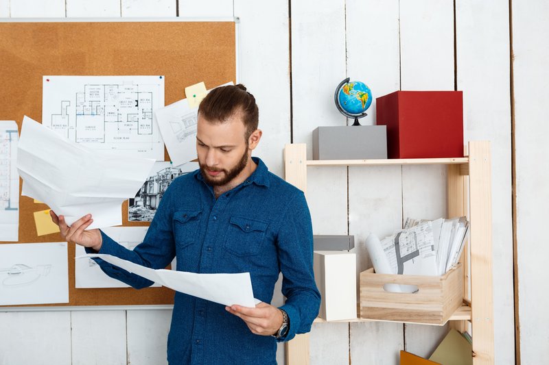 young-successful-architector-looking-drawings-standing-office (1)